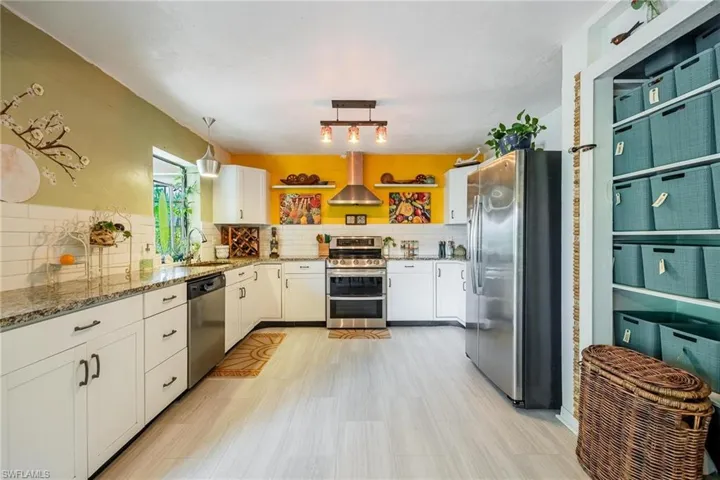 Kitchen with hanging light fixtures, appliances with stainless steel finishes, decorative backsplash, and wall chimney exhaust hood