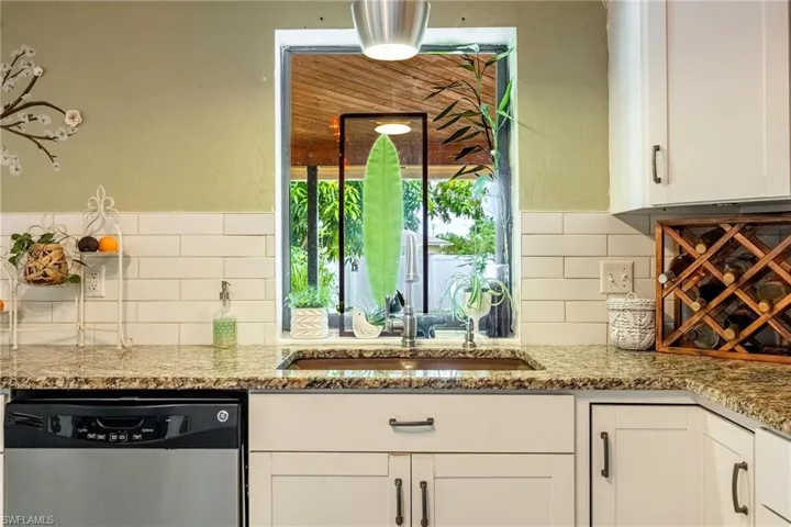 Kitchen featuring white cabinets, light stone counters, decorative backsplash, and stainless steel dishwasher