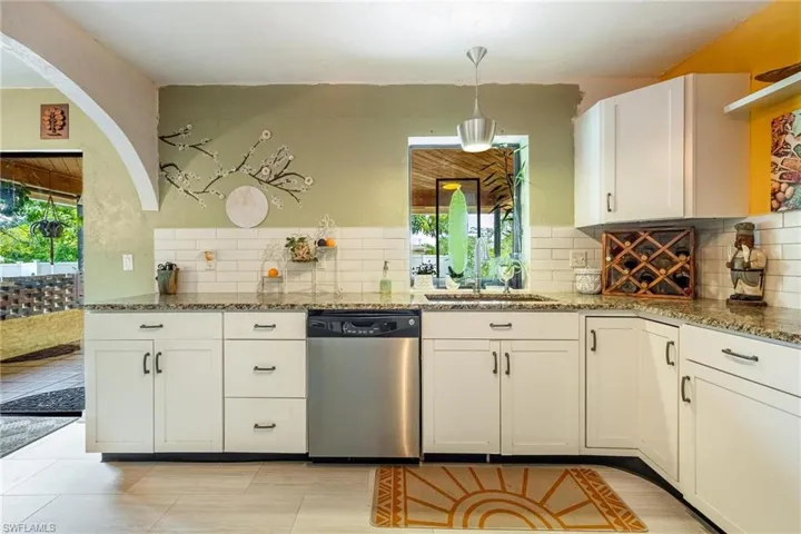 Kitchen with stone countertops, a healthy amount of sunlight, stainless steel dishwasher, and decorative backsplash