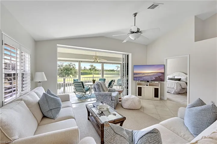 Vaulted ceilings, large-format tile flooring, multi-panel sliding glass doors, white plantation shutters, and ceiling fan