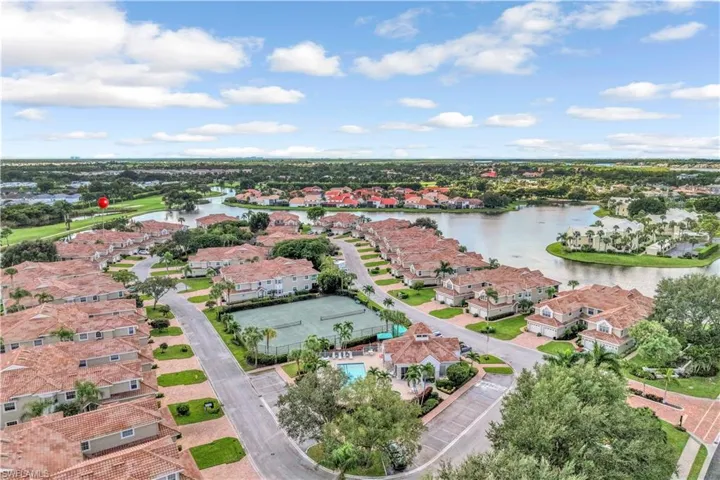 Aerial perspective of a residential community featuring tile roofs, a central swimming pool, tennis courts, and waterfront landscaping