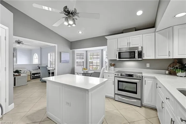 Kitchen featuring white cabinetry, an island with a light-toned countertop, stainless steel appliances, tile flooring, and a vaulted ceiling