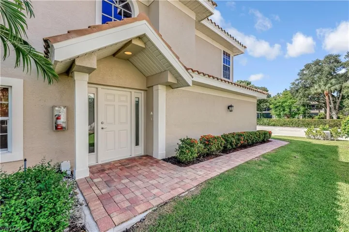Covered entryway featuring a peaked roofline, stucco exterior, paver walkway, and arched decorative window