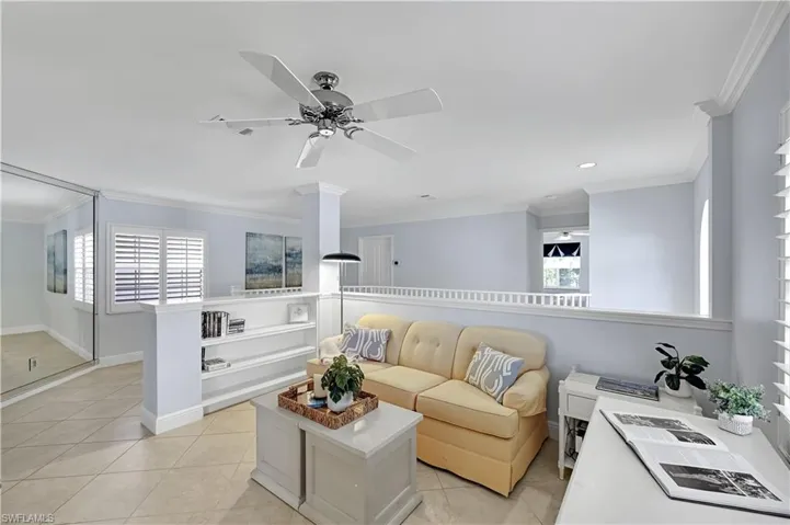 Open-concept space featuring tile flooring, built-in shelving, a ceiling fan, crown molding, and a floor-to-ceiling mirrored wall