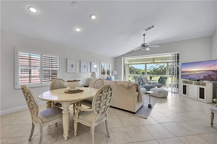 Open-concept interior featuring vaulted ceilings, recessed lighting, tile flooring, plantation shutters, and sliding glass doors leading to a screened-in lanai