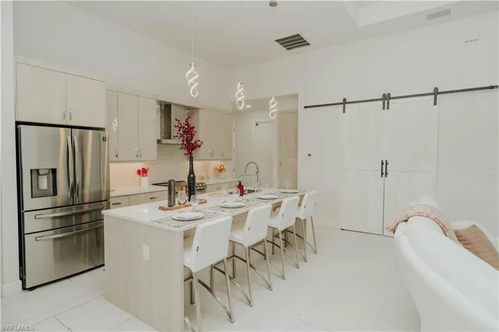 Kitchen with decorative light fixtures, visible vents, light countertops, stainless steel refrigerator with ice dispenser, and a center island with sink