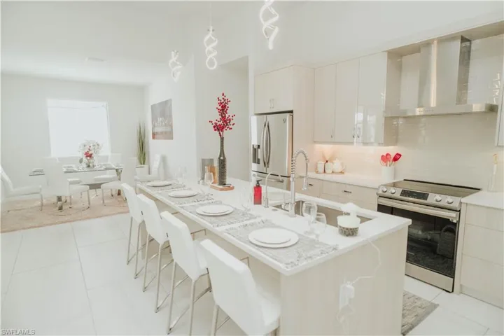 Kitchen featuring stainless steel appliances, white cabinets, light countertops, wall chimney exhaust hood, and tasteful backsplash