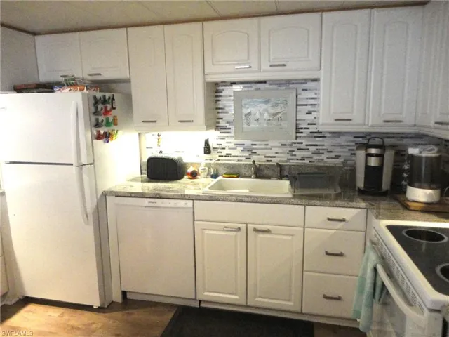 Kitchen with white cabinets, backsplash, white appliances, and sink