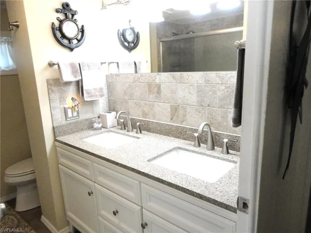 Guest Bathroom featuring vanity, toilet, a shower with shower door, and tasteful backsplash