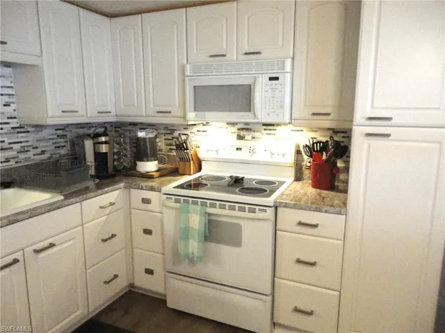 Kitchen with backsplash, sink, white cabinets, and white appliances