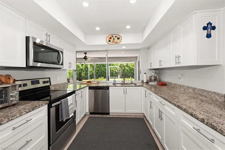 U-shaped kitchen featuring white shaker cabinetry, stainless steel appliances, speckled stone countertops, and recessed lighting