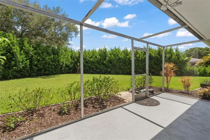 Screened lanai featuring a concrete surface, overhead lighting, and access to a landscaped backyard