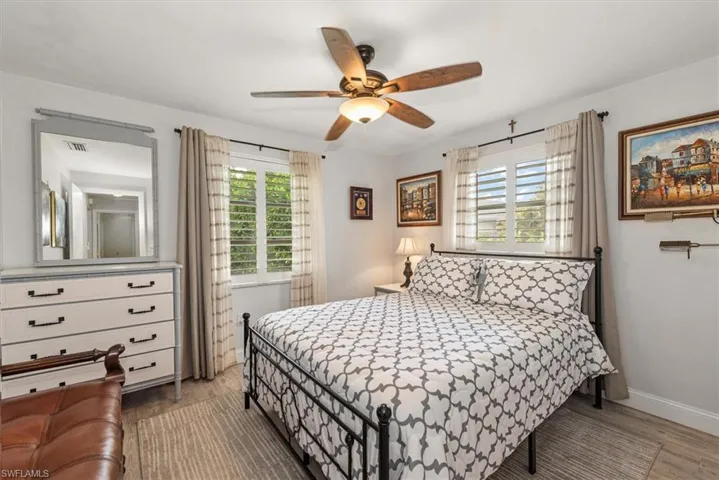 Bright room featuring two windows with white plantation shutters, a ceiling fan with light fixture, and wood-finish flooring