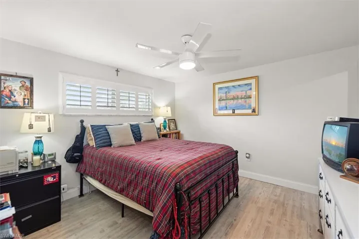 Interior room featuring light-toned wood-finish flooring, a white ceiling fan with integrated lighting, and plantation shutters on a window