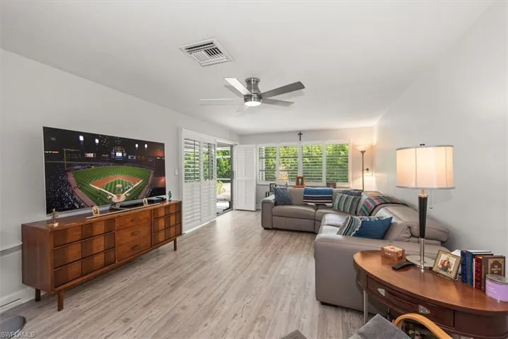Spacious living area featuring light wood-finish flooring, white walls, and a modern ceiling fan