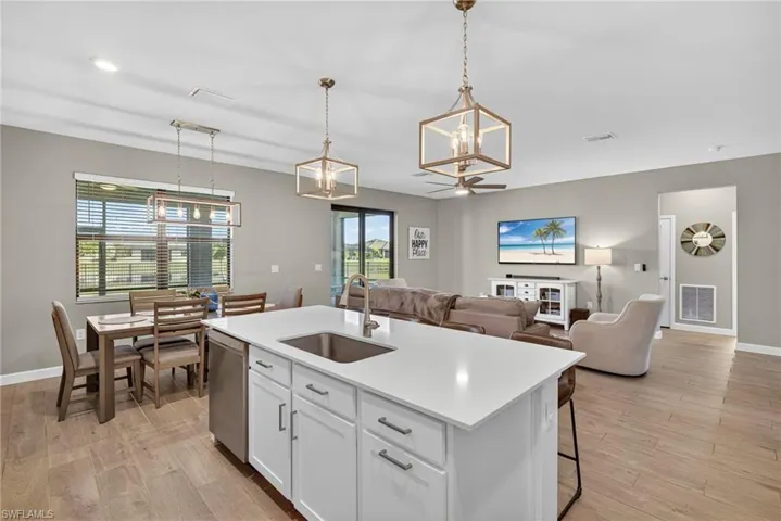 Kitchen with white cabinetry, decorative light fixtures, a kitchen island with sink, and light wood finished floors
