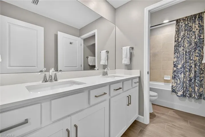 Full bath with wood tiled floors, shower / bath combination with curtain, and double vanity