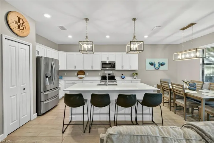 Kitchen featuring stainless steel appliances, hanging light fixtures, a kitchen breakfast bar, white cabinets, and a center island with sink