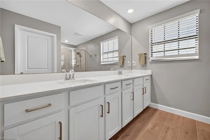 Bathroom with wood finish floors, double vanity, a shower stall, and recessed lighting