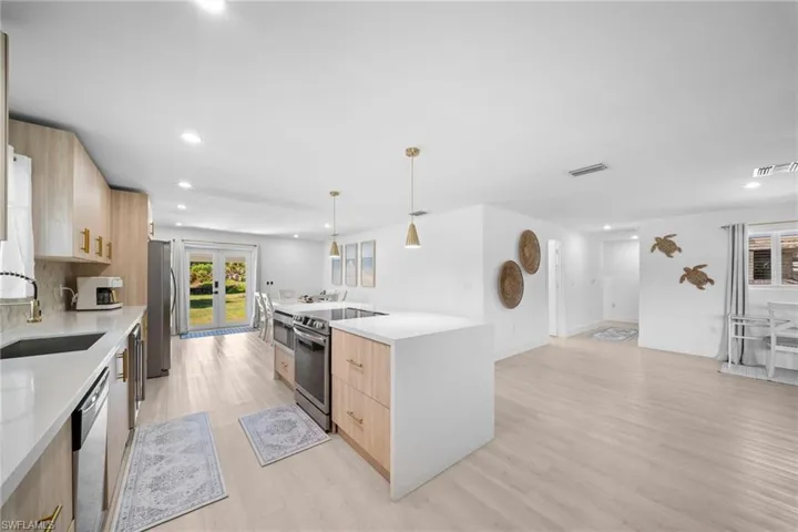 Kitchen featuring light wood-finish cabinetry, quartz countertops, a central island with integrated stainless steel appliances, and wood-finish flooring