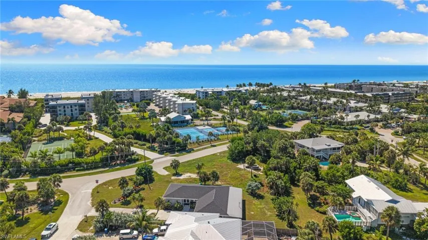 Aerial perspective of a coastal community featuring paved streets, mature palm trees, multi-story buildings, and recreational courts