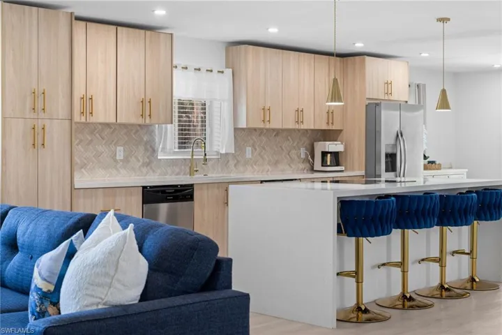 Kitchen featuring light wood-finish cabinetry, quartz countertops, a herringbone-patterned tile backsplash, a central island with waterfall edges, and gold-tone pendant lighting
