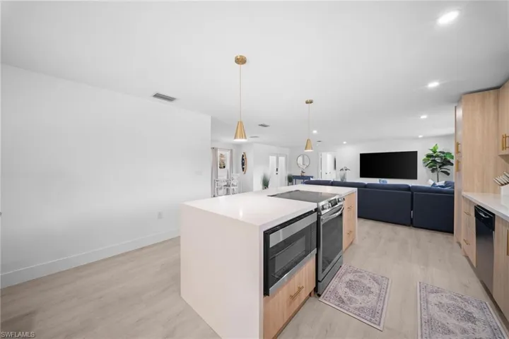 Kitchen island featuring a stone-finish countertop, stainless steel cooktop, integrated microwave, wood-finish cabinetry with brass hardware, and dual pendant lighting