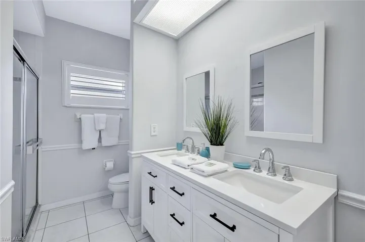 Full bathroom with double sink vanity, a stall shower, and toilet