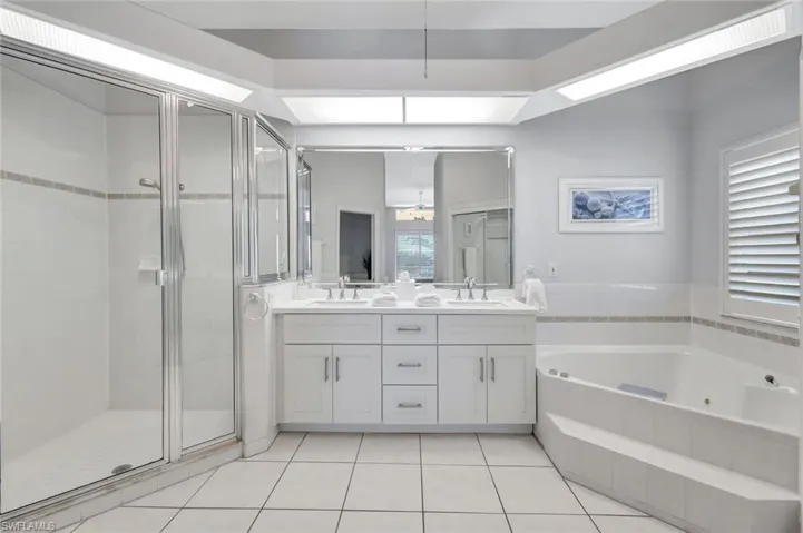 Full ensuite bathroom with a sink, a whirlpool tub, a stall shower, and double vanity