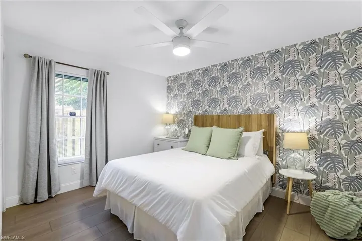 Bedroom with wallpapered walls, dark wood-style flooring, an accent wall, and a ceiling fan