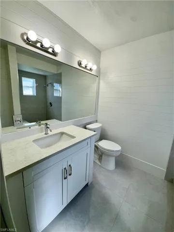 Full bath featuring vanity, wooden walls, and dark tile patterned flooring