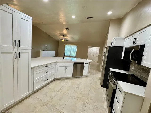 Kitchen with lofted ceiling, white cabinets, appliances with stainless steel finishes, light stone counters, and backsplash