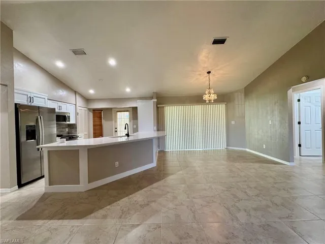 Kitchen featuring stainless steel appliances, white cabinetry, pendant lighting, a spacious island, and a chandelier