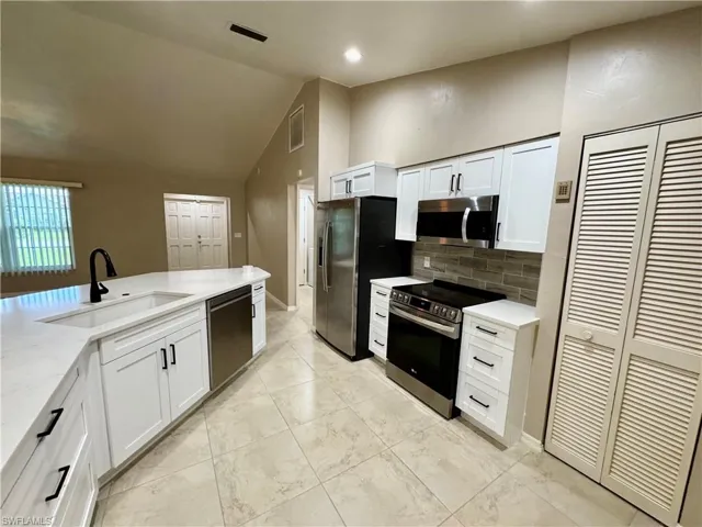Kitchen with lofted ceiling, appliances with stainless steel finishes, white cabinetry, tasteful backsplash, and light stone counters