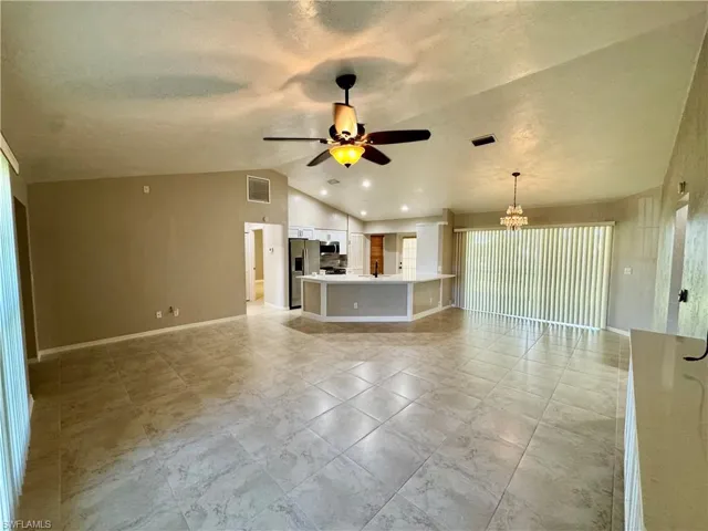 Unfurnished living room with lofted ceiling, a textured ceiling, a chandelier, and ceiling fan
