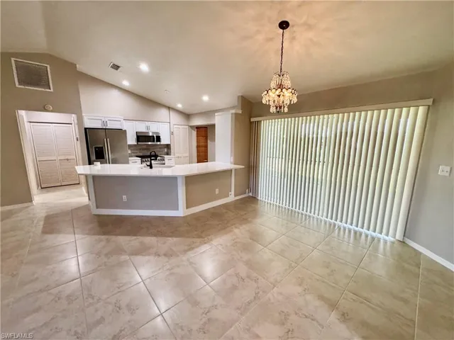 Kitchen with a peninsula, stainless steel appliances, vaulted ceiling, white cabinets, and pendant lighting