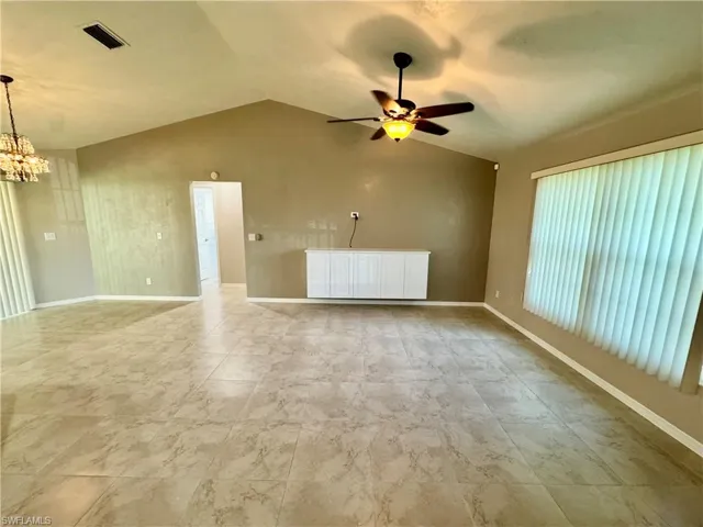 Unfurnished living room with vaulted ceiling, a ceiling fan, and a chandelier