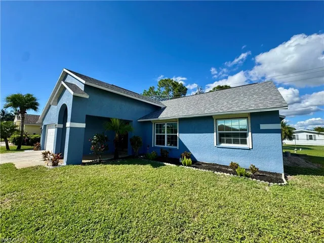 Ranch-style home with a front yard, stucco siding, roof with shingles, and driveway