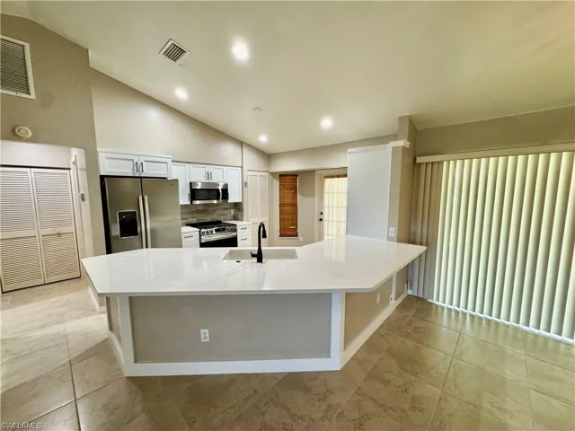 Kitchen with lofted ceiling, white cabinets, backsplash, appliances with stainless steel finishes, and light stone countertops