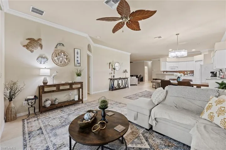 Open-concept living area with light-toned wall finishes, crown molding, a decorative ceiling fan, and recessed lighting