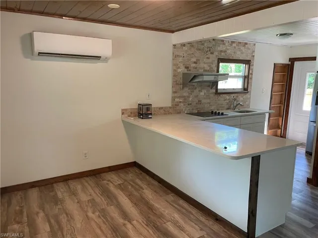 Kitchen with wooden ceiling, a peninsula, dark wood finished floors, a wall mounted air conditioner, and freestanding refrigerator