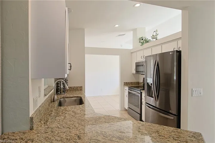 Kitchen featuring speckled stone countertops, stainless steel appliances, white cabinetry, and recessed lighting