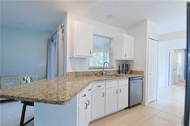Kitchen featuring L-shaped stone-finish countertops, white cabinetry with black hardware, and an undermount stainless steel sink