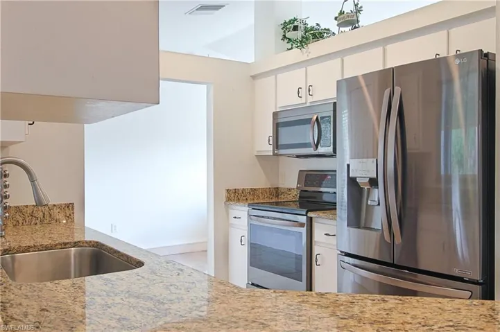 Kitchen featuring light-toned countertops, white cabinetry, a stainless steel undermount sink with a high-arch faucet, a stainless steel French door refrigerator, and stainless steel built-in appliances