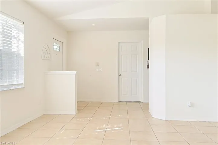 Bright interior space with light-toned square tile flooring, neutral wall finishes, and a window featuring horizontal blinds