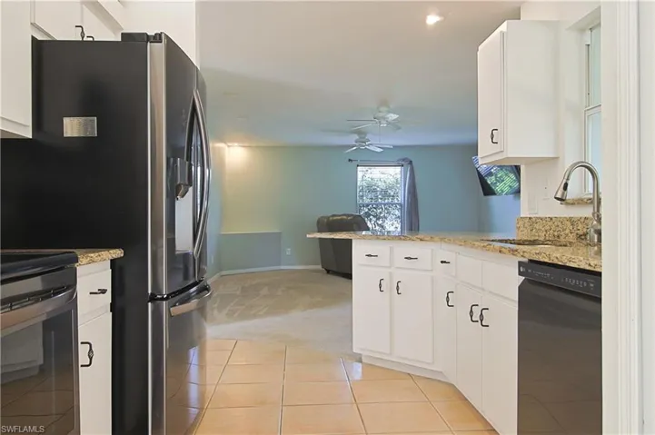 Kitchen featuring white cabinetry, light-toned countertops, tile flooring, and a black appliance suite with a stainless steel refrigerator