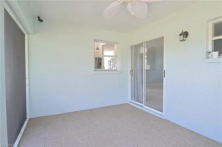 Screened patio featuring a ceiling fan, sliding glass doors, and textured exterior walls