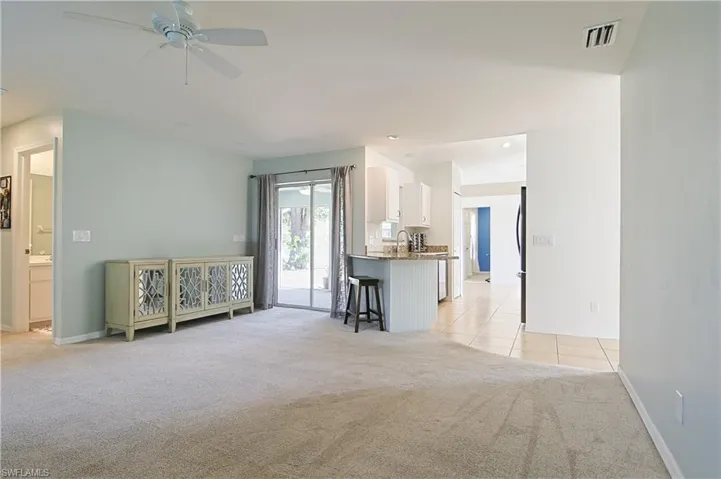 Spacious carpeted living area with a ceiling fan, light-toned walls, and sliding glass doors to the exterior