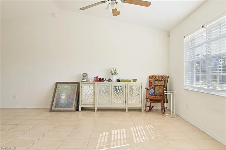 Spacious room with vaulted ceilings and a ceiling fan, featuring large windows with blinds, and light-toned tile flooring