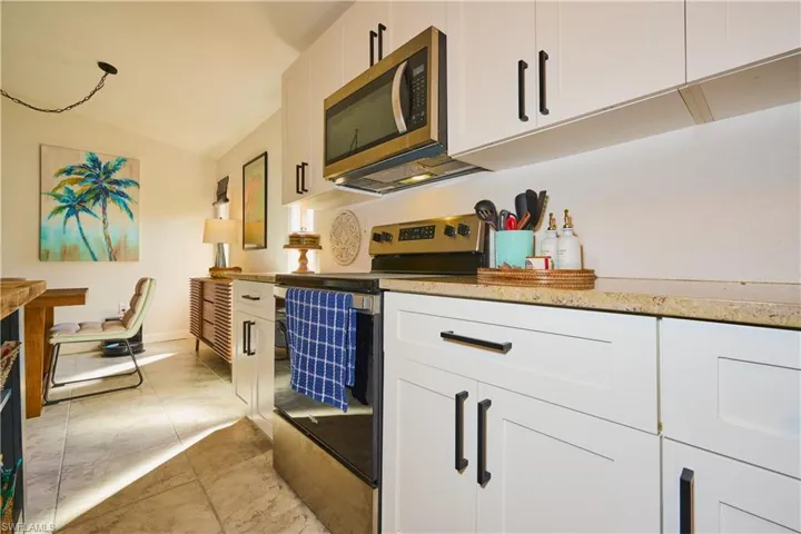 Kitchen featuring white shaker-style cabinetry, stone-finish countertops, stainless steel appliances, and tile flooring